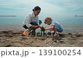 A happy mother and her little child enjoy a warm day at the beach, playing with sand and water. They spend quality time together, creating lasting memories. 139100254