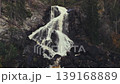 Drone footage of a waterfall cascading down a rock face, captured from a horizontal perspective. 139168889