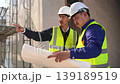 Two engineers discuss blueprints on a construction site ensuring project details are clearly understood. 139189519