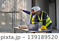 Engineers discuss project details at a construction site ensuring efficient collaboration for successful completion. 139189520