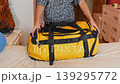 Person unpacking large travel duffel bag after hiking trip at home, sorting outdoor gear and equipment on bed, post adventure routine, travel unpacking and organization process indoors  139295772