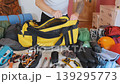 Man packing large duffel bag with climbing equipment and clothing, organizing gear on bed before hiking or mountaineering trip, preparation process for outdoor adventure at home 139295773