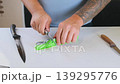 Man sharpening knife using whetstone on table, maintaining blade edge with manual sharpening technique, tool care and maintenance process at home, close up of hands and cutting tools 139295776