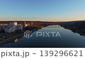 Smooth rightward aerial drone pan over riverside cityscape at sunset with reflections and warm illuminated buildings. Concept of calm urban evening atmosphere and harmony between architecture 139296621
