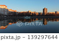 Smooth rightward aerial drone pan over riverside cityscape at sunset with reflections and warm illuminated buildings. Concept of calm urban evening atmosphere and harmony between architecture 139297644