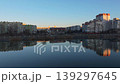 Smooth rightward aerial drone pan over riverside cityscape at sunset with reflections and warm illuminated buildings. Concept of calm urban evening atmosphere and harmony between architecture 139297645