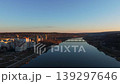 Smooth rightward aerial drone pan over riverside cityscape at sunset with reflections and warm illuminated buildings. Concept of calm urban evening atmosphere and harmony between architecture 139297646