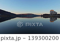 Smooth rightward aerial drone pan over riverside cityscape at sunset with reflections and warm illuminated buildings. Concept of calm urban evening atmosphere and harmony between architecture 139300200