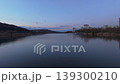 Smooth rightward aerial drone pan over riverside cityscape at sunset with reflections and warm illuminated buildings. Concept of calm urban evening atmosphere and harmony between architecture 139300210