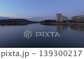 Smooth rightward aerial drone pan over riverside cityscape at sunset with reflections and warm illuminated buildings. Concept of calm urban evening atmosphere and harmony between architecture 139300217