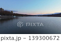 Smooth rightward aerial drone pan over riverside cityscape at sunset with reflections and warm illuminated buildings. Concept of calm urban evening atmosphere and harmony between architecture 139300672
