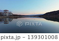 Smooth rightward aerial drone pan over riverside cityscape at sunset with reflections and warm illuminated buildings. Concept of calm urban evening atmosphere and harmony between architecture 139301008
