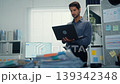 Thoughtful young Latin businessman stand with laptop analyzing data above paperwork stack. Hybrid work audit, digital transformation strategy, business corporate finance, executive decision concept. 139342348