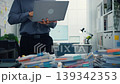 Thoughtful young Latin businessman stand with laptop analyzing data above paperwork stack. Hybrid work audit, digital transformation strategy, business corporate finance, executive decision concept. 139342353