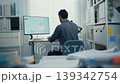 Rear view of young Latin businessman analyzing financial graph data on computer screen in office with paperwork. Hybrid work, fintech strategy, corporate performance, and market statistics concept. 139342754