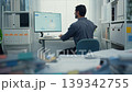 Rear view of young Latin businessman analyzing financial graph data on computer screen in office with paperwork. Hybrid work, fintech strategy, corporate performance, and market statistics concept. 139342755
