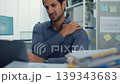Young Latino businessman suffering shoulder pain and neck ache at office desk with computer. Office syndrome, muscle massage, overworked stress, bad posture, and health insurance injury concept. 139343683