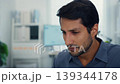 Stressed young Latin businessman having severe headache and migraine at office desk. Debt crisis, corporate burnout, mental health anxiety, business failure, and work financial frustration concept. 139344178