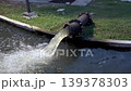 Water discharges from a large metal pipe into a canal, creating splashes and turbulence, industrial drainage system in outdoor setting, infrastructure managing flow, environmental and utility concept 139378303