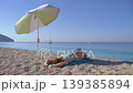 Female resting on beach towel under umbrella. Calm 139385894