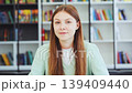 Happy young female student celebrating success or good news in library. Excited woman looking at camera and cheering with raised hands in room 139409440