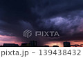 Dramatic dark storm clouds swirling over a city skyline at sunset. Epic purple and orange sky with heavy rain and wind. Ominous urban weather phenomenon 139438432