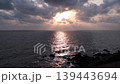 As the day begins its soft descent, the heavens part to reveal a celestial radiance burning through a tapestry of charcoal and violet clouds. This golden aperture casts down ethereal rays fingers. 139443694