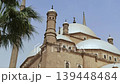 Low angle view of Muhammad Ali Mosque domes, minarets and crescent finials at Cairo Citadel, Egypt, with palm tree framing Ottoman Islamic architecture against hazy purple sky. 139448484
