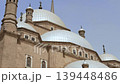 Low angle view of Muhammad Ali Mosque domes, minarets and crescent finials at Cairo Citadel, Egypt, with palm tree framing Ottoman Islamic architecture against hazy purple sky. 139448486