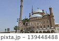 Daylight view of Muhammad Ali Mosque grand exterior, Cairo, Egypt, sandstone walls, white marble domes, tall fluted minaret and arched loggia with palm trees. 139448488