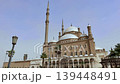 Stunning Ottoman mosque with gleaming white domes and towering minaret at Cairo Citadel, Egypt, elegant arched gallery and palm trees in sunny clear weather. 139448491