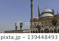 Exterior view of historic Muhammad Ali Mosque at Saladin Citadel, Cairo, Egypt, featuring layered Ottoman domes, tall minaret and graceful arcade under bright blue sky. 139448493