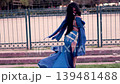Sensual Latina woman dancing belly dance, twirling in slow motion and having fun, wearing a beautiful blue dress, in a park at sunset, with makeup. Dancing and smiling, with sensuality and joy. 139481488