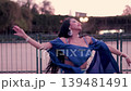 Sensual Latina woman dancing belly dance in a park at sunset, wearing a blue dress, swaying, moving her hands, and wearing makeup. Dancing and smiling, with sensuality and joy. 139481491