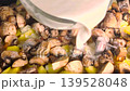 Chef pouring white creamy sauce over raw sliced potatoes and mushrooms in a baking dish. 139528048