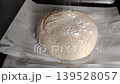 Baker sprinkling white flour over raw sourdough bread dough on parchment paper before baking. 139528057
