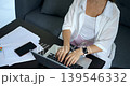 Female typing at desk. Lady composing report with devices nearby. Woman focused on writing report using multiple gadgets. Individual engaged in data entry in cozy home workspace setting 139546332