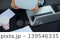 Organizing papers now. Arranging documents on workspace diligently. Sorting and annotating files at tidy desk station. Carefully managing paperwork alongside cup of coffee and electronic devices 139546335