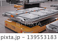 Orbit around Lithium-Ion Battery Module loaded on AGV inside Fully Automated Modern Car Factory. AI-powered Humanoid Robots and Automated Guided Vehicles moving in Background. 3d Animation Render 139553183