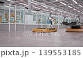 Camera moves through AGVs loaded with Electric Car Chassis in Fully Automated Modern Autonomous Electric Car Factory. AI-powered Humanoid Robots and Robotic Arms in Background. 3d Animation Render 139553185