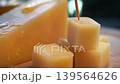 Close up shows skewer entering cube of cheese while hand lifts it from cutting board. Golden tones and blurred background emphasize fresh snack preparation. 139564626