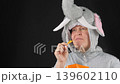 Middle-aged woman in an elephant costume eating potato chips. In a good mood. Enjoying. On a black background. 139602110