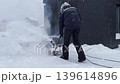 man clearing snow near wooden house in countryside using electric snow blower 139614896