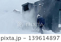 man clearing snow near wooden house in countryside using electric snow blower 139614897