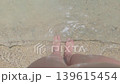 A first person perspective bare female feet in the foaming waves on a light sand beach with small pebbles and shells on a sunny, bright day. Active lifestyle during vacations, holidays, and weekends 139615454