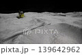 Beneath a dark sky, astronauts work near a lunar lander on the moons surface. The rugged terrain features craters and a stark, desolate landscape, capturing a moment of space exploration. 139642962