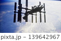 A large space station hovers in low Earth orbit, showcasing its solar panels and structure. Below, a view of Earth reveals fluffy clouds against the dark expanse of space. 139642967