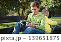 Brothers sitting on park bench engrossed in their smartphones, highlighting smartphone addiction. Concept of technology dependence 139651875
