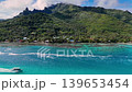 Turquoise lagoon at Moorea with speedboat cutting white wake beneath jagged volcanic peaks, aerial view of coral reef patches, shoreline village, lush rainforest ridges Moorea, French Polynesia 139653454