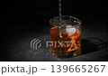 Bartender stirring cocktail ingredients in a whiskey glass filled with ice in an extreme close-up shot against a dark background   139665267